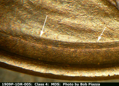 Die-stage B marker on 1909P•1DR•005 showing thin parallel die scratches run across the truncation of the bust under the shoulder.
