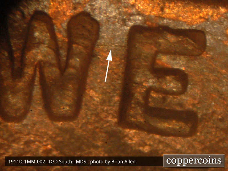 Die-stage B marker on 1911D•1MM•002 showing Other concentric die scratches show between the W and E of WE.