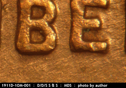 Die-stage B marker on 1911D•1OM•001 showing A small die scratch points eastward from the lowed section of the B to the E of LIBERTY.