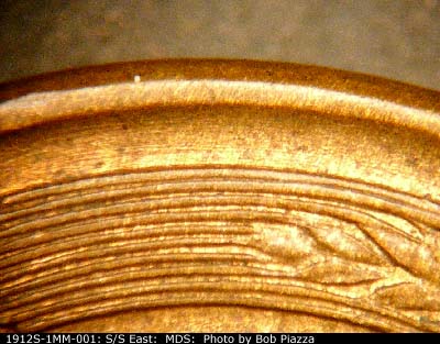 Die-stage B marker on 1912S•1MM•001 showing Many fine die scratches run concentric to the outside of the right wheat.