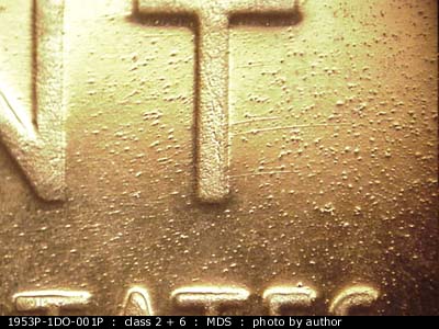 Die-stage B marker on 1953P•1DO•001P showing A patch of E to W die scratches shows around the tee of scent.