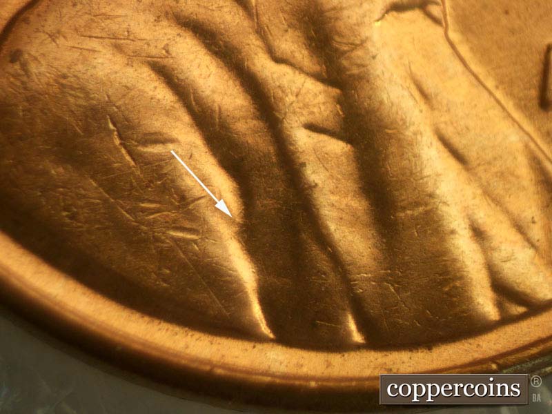 Die-stage B marker on 1960D•1MM•003 showing NE die scrathch in shoulder fold.
