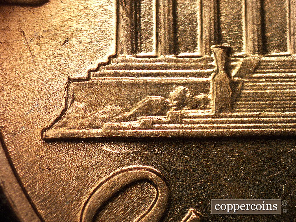 Die-stage D marker on 1960D•1MM•003 showing A die chip shows on the left base, and a depression with die crack shows along the bottom of the left base.