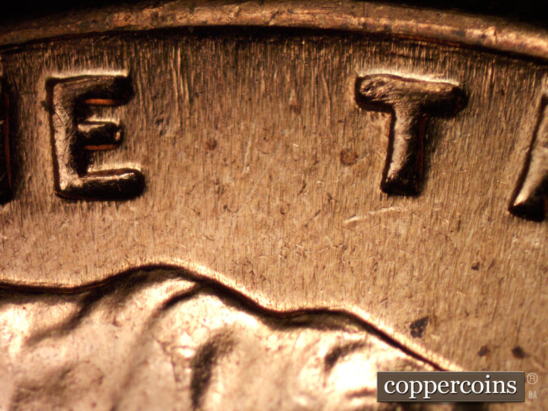 Die-stage B marker on 1960D•1MM•004 showing Die scratch above first T in TRUST.
