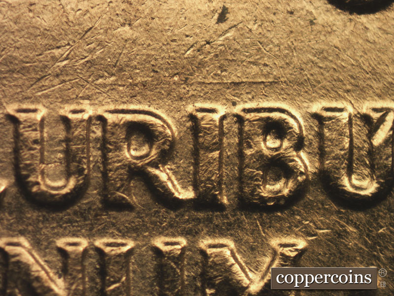 Die-stage B marker on 1960D•1MM•016 showing E/W die scratch above RIB in PLURIBUS.