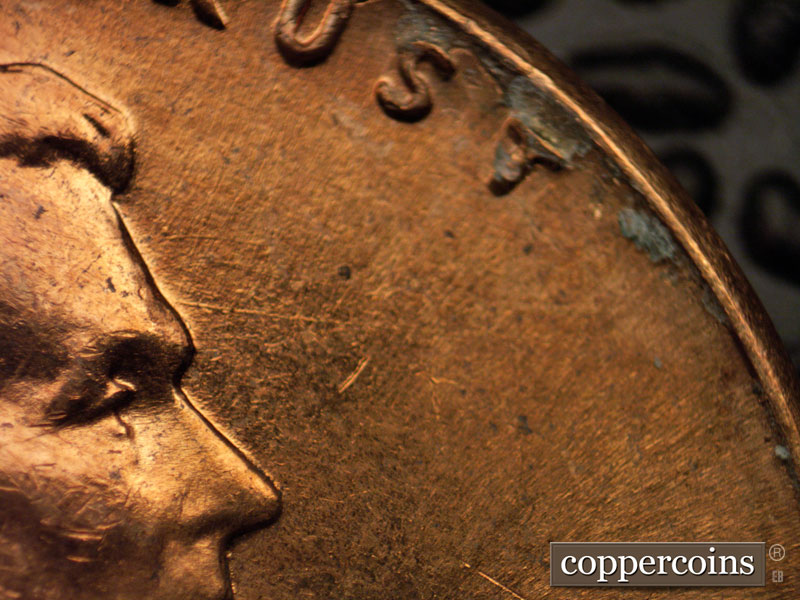 Die-stage A marker on 1960D•1MM•027 showing ESE die scratch from forehead toward rim.
