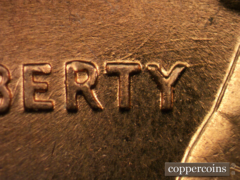 Die-stage C marker on 1960D•1MM•050 showing Group of worn curved die scratches through and above RTY in LIBERTY.