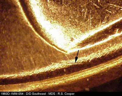 Die-stage B marker on 1960D•1MM•054 showing Die scracth between back corner of shoulder and rim.