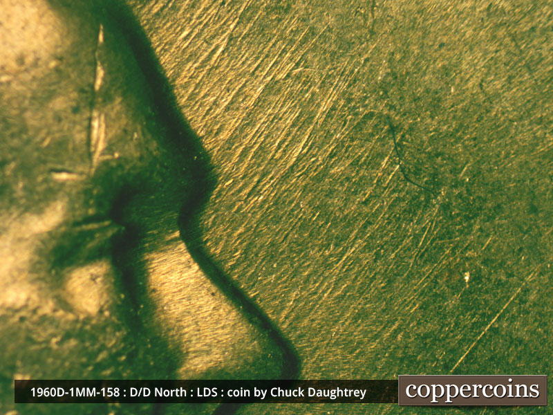Die-stage D marker on 1960D•1MM•158 showing NE die scratches from forehead and nose.