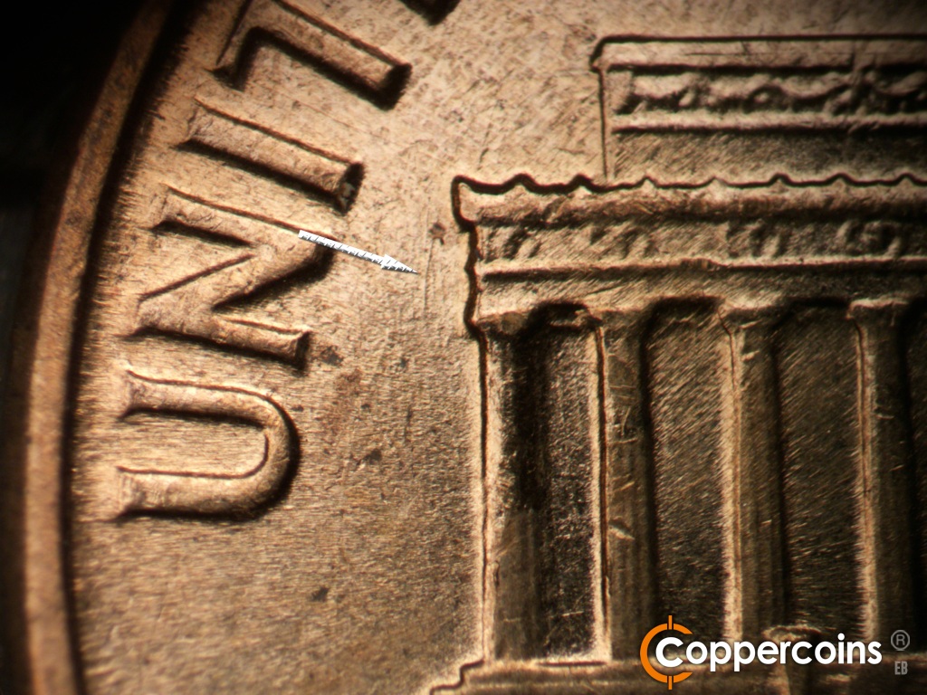 Die-stage B marker on 1961D•1MM•021 showing Die scratch in field west of left cornice.