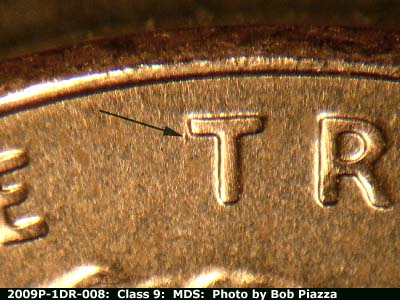 Die-stage B marker on 2009P•1DR•008 showing A small die gouge to the left of the horizontal crossbar of the first T of TRUST.