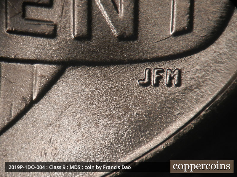 Die-stage B marker on 2019P•1DO•004 showing A die scratch runs horizontally through JFM. A die crack also extends southwest from the bottom of the T in CENT.