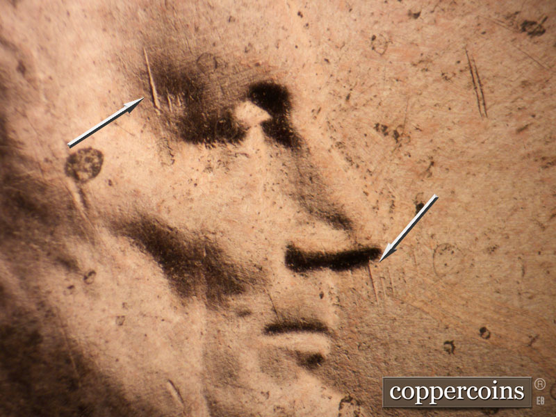 Die-stage A marker on 2021P•1DR•001 showing N/S die gouges on temple and from nose.