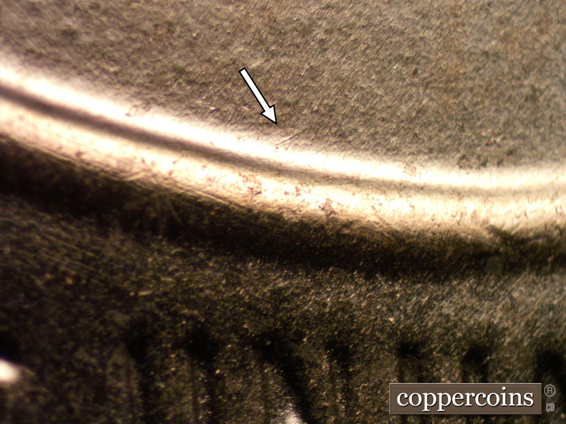 Die-stage B marker on 2024D•1DO•002 showing NE die scratch from the top of shield.
