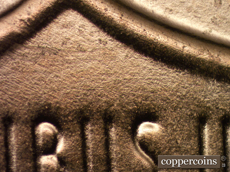 Die-stage B marker on 2024D•1DO•002 showing E/W die scratches above BUS in PLURIBUS.
